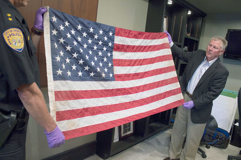 Everett Mayor Ray Stephanson (right) and Deputy Police Chief Mark St. Clair help display a flag that is believed to be linked to a famous photo of ground zero in New York after the Sept. 11, 2001, terrorist attacks. The flag turned up in Everett in 2014 when an unidentified man dropped it off at a fire station. (City of Everett)
