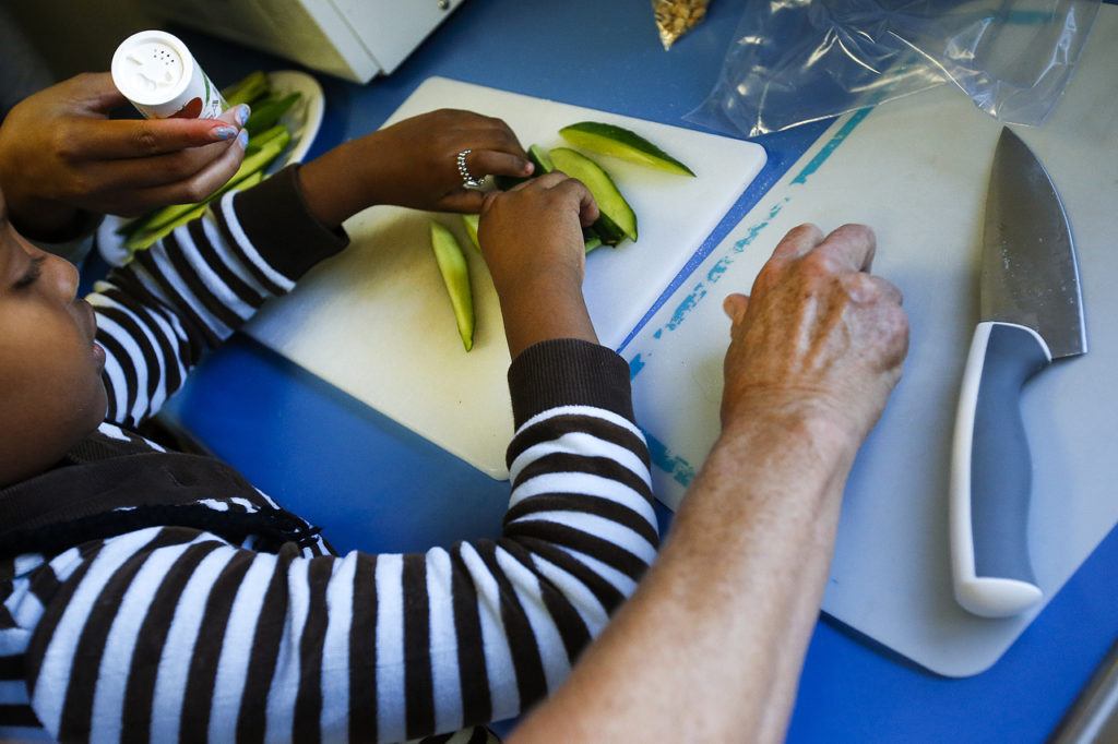 Lisa Sheja, 6, divides up cucumber slices after cutting them with the help of volunteer Pat Benefiel before sprinkling on a little salt at the East Casino Road YMCA in Everett on Tuesday, Sept. 20. (Ian Terry / The Herald)
