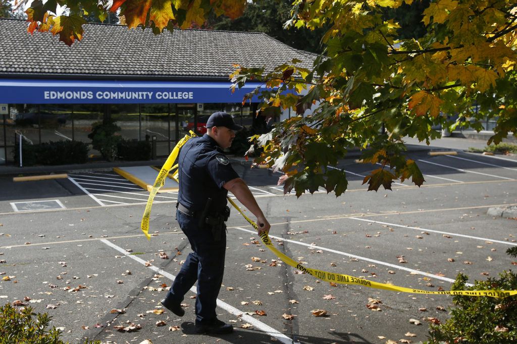 An officer with the Mill Creek Police Department clears away police tape after a suspicious device found in an impounded car was deemed benign on Thursday morning near the north end of Edmonds Community College campus. (Ian Terry / The Herald)
