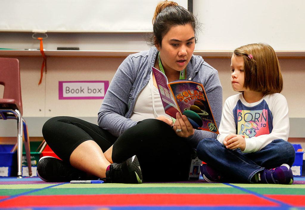 Hawthorne Elementary kindergarten teacher Diane Barnett joins the Day of Caring effort and reads to Lily Losier while other volunteers read to kids in her classroom Friday. (Dan Bates / The Herald)
