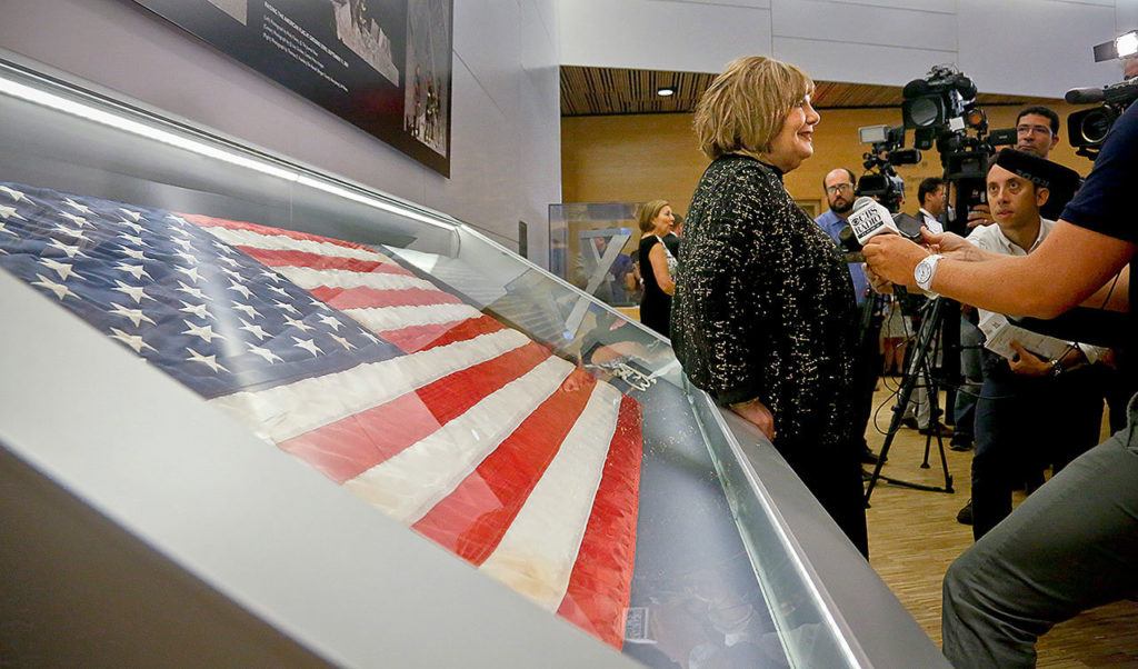 Shirley Dreifus, center, the original owner of the American flag, left, that firefighters hoisted at ground zero in the hours after the 9/11 terror attacks, hold interviews at the Sept. 11 museum, Thursday in New York. After disappearing for more than a decade, the 3-foot-by-5-foot flag goes on display Thursday at the museum. (AP Photo/Bebeto Matthews)
