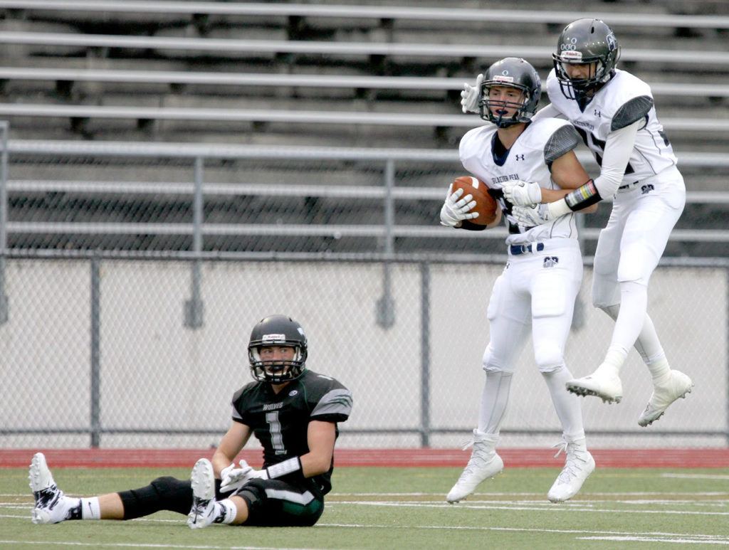 Glacier Peak’s Heston Pettis (standing left) celebrates with teammate Bo Burns after Pettis’ interception from a pass intended for Jackson’s Jackson Hering (left) during a game Friday night at Everett Memorial Stadium. (Kevin Clark / The Herald)
