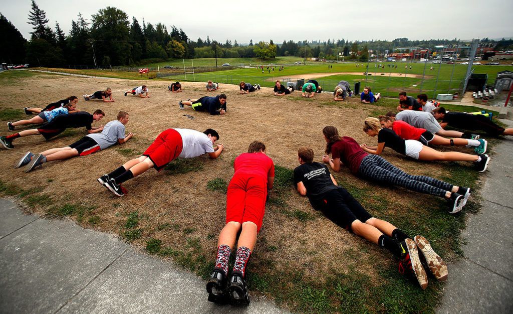 Led by instructor Matt Gale (center), a freshman PE class rests between sets of push-ups on the lawn between the school buildings and practice fields Thursday. (Dan Bates / The Herald)
