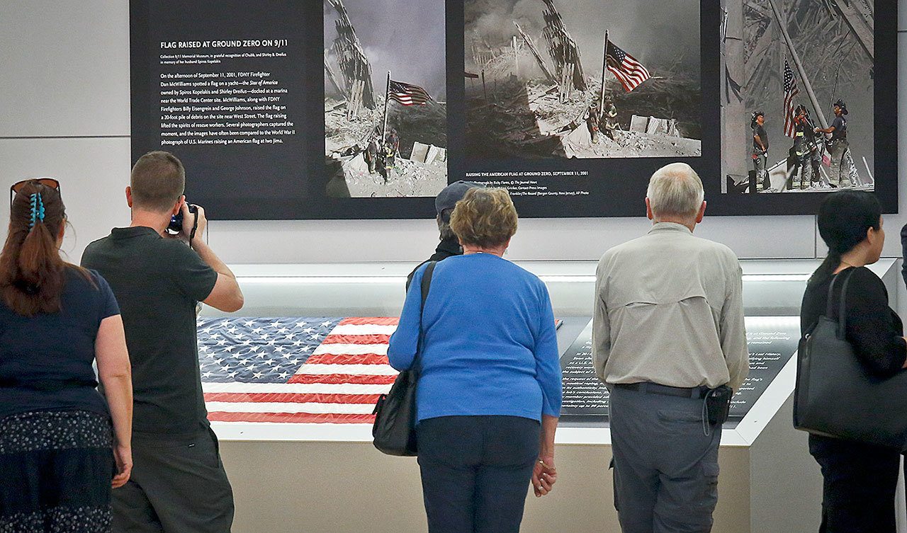 Visitors view the display for the American flag, left, that firefighters hoisted at ground zero in the hours after the 9/11 terror attacks, Thursday at the Sept. 11 museum in New York. After disappearing for more than a decade the 3-foot-by 5-foot flag was donated to the museum after it was turned in two years ago by an as-yet-unidentified man at a firehouse in Everett, Washington. (AP Photo/Bebeto Matthews)
