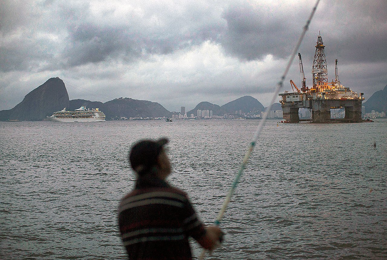 In this 2015 photo, a man fishes in Guanabara Bay where an oil platform floats, backdropped by Sugar Loaf Mountain, left, in Niteroi, Brazil. The Brazilian government on Monday ratified its participation in the Paris Agreement on climate change, a significant step by Latin America’s largest emitter of greenhouse gases that could spur other countries to move forward. (AP Photo/Leo Correa, File)