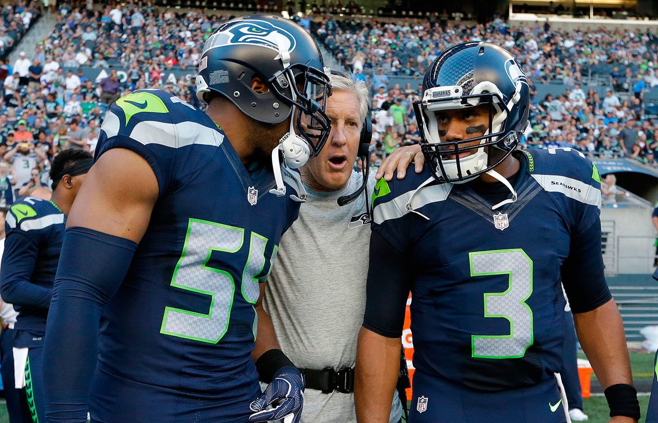 Seattle Seahawks head coach Pete Carroll, center, talks to Bobby Wagner, left, and Russell Wilson, right, before a preseason NFL football game against the Minnesota Vikings on Aug. 18 in Seattle. (AP Photo/Elaine Thompson)