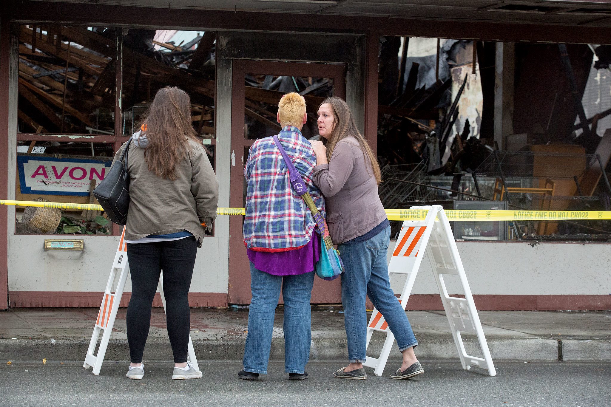 Laina Lundgren, right, puts a hand on the shoulder of 2 Bits and More owner Dawn Ambler as they look over the remains of the indoor flea market and thrift shop after a fire the night before on Tuesday, Oct. 25, 2016 in Arlington, Wa. At left is Ambler’s niece Jeness Crtiz. (Andy Bronson / The Herald)