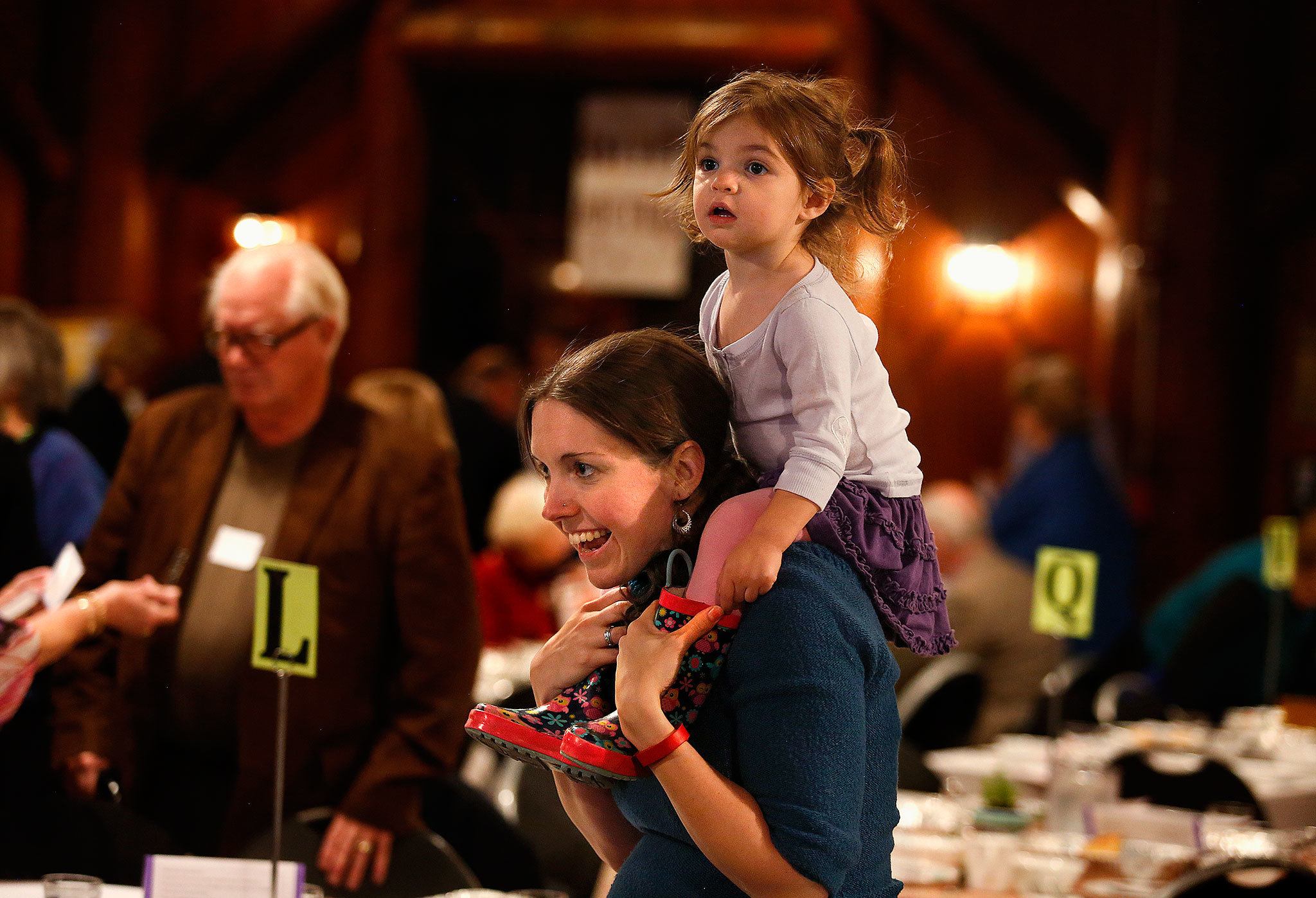 Oh, what a night! Cathy Merchant, of Redmond, carries her 2-year-old daughter, Inara, on her shoulders as she negotiates a big crowd while attending a fundraiser for the Interfaith Association’s family shelter, at Forest Park’s Floral Hall on Wednesday. (Dan Bates / The Herald)