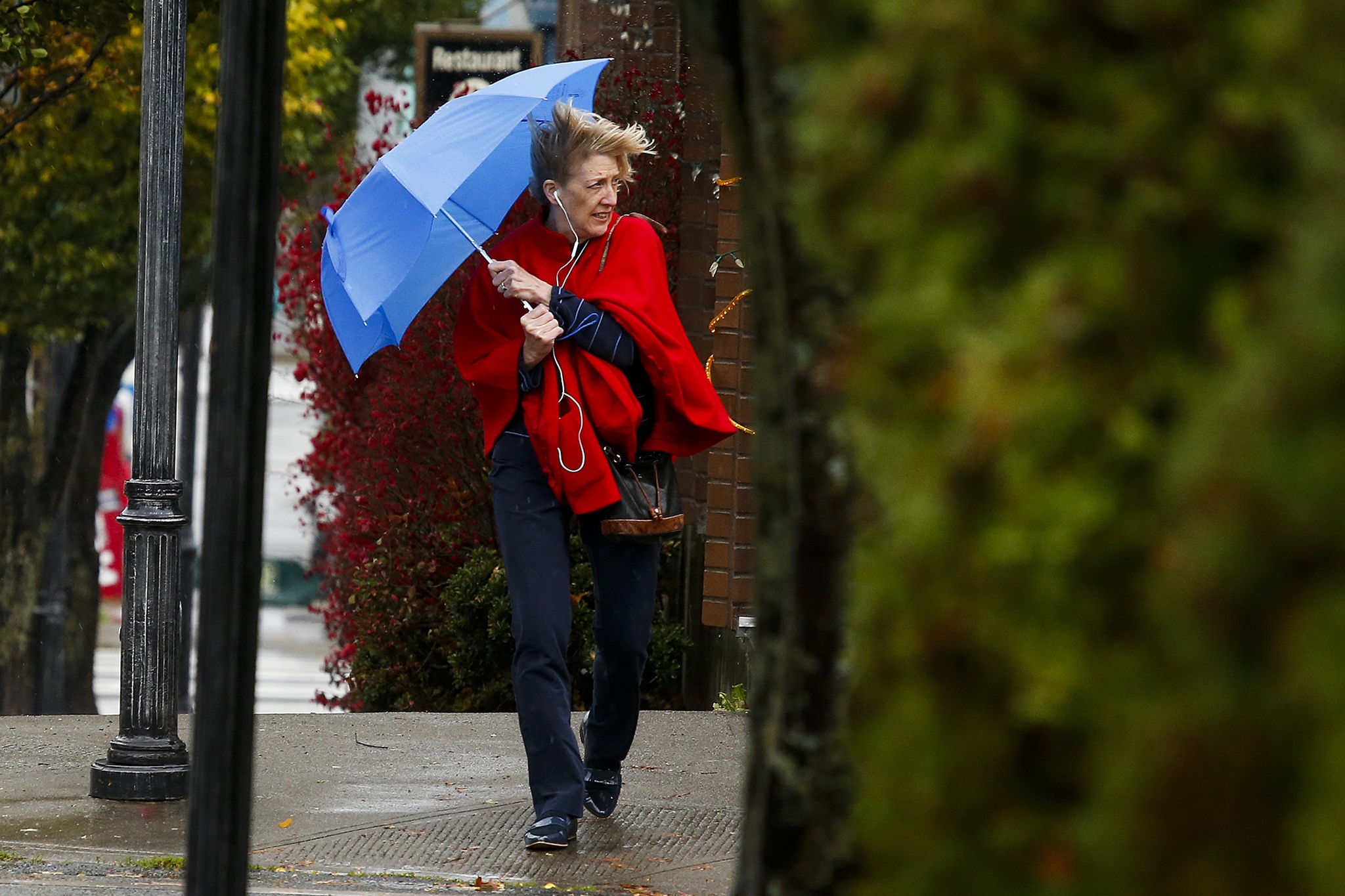 A pedestrian uses an umbrella to shield herself from the wind as she crosses 2nd Avenue North near Main Street in downtown Edmonds on Friday afternoon. (Ian Terry / The Herald)