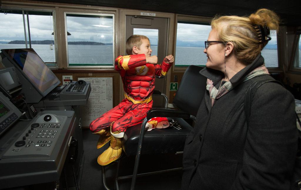 As his mother, Michelle, watches, the Flash (aka Jayden Darnell, 8) pretends to drive the ferry backwards while touring the bridge of the M/V Chelan during the Washington State Ferries’ first Halloween Costume Contest on Monday, Oct. 31. Crews on ferries picked costume winners from the walk-ons and then escorted one winner to the bridge for the duration of the run. (Andy Bronson / The Herald)
