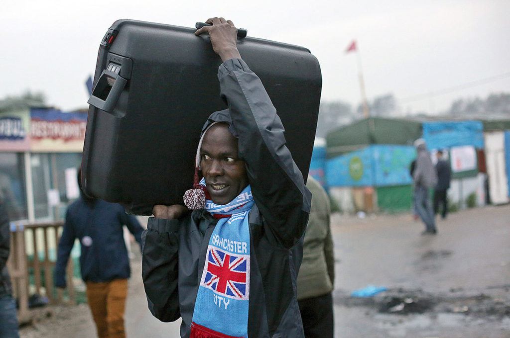 An unidentified migrant carrying his luggage leaves a makeshift camp known as “the jungle” near Calais, northern France, to register at a processing center on Monday Oct. 24. (AP Photo/Thibault Camus)
