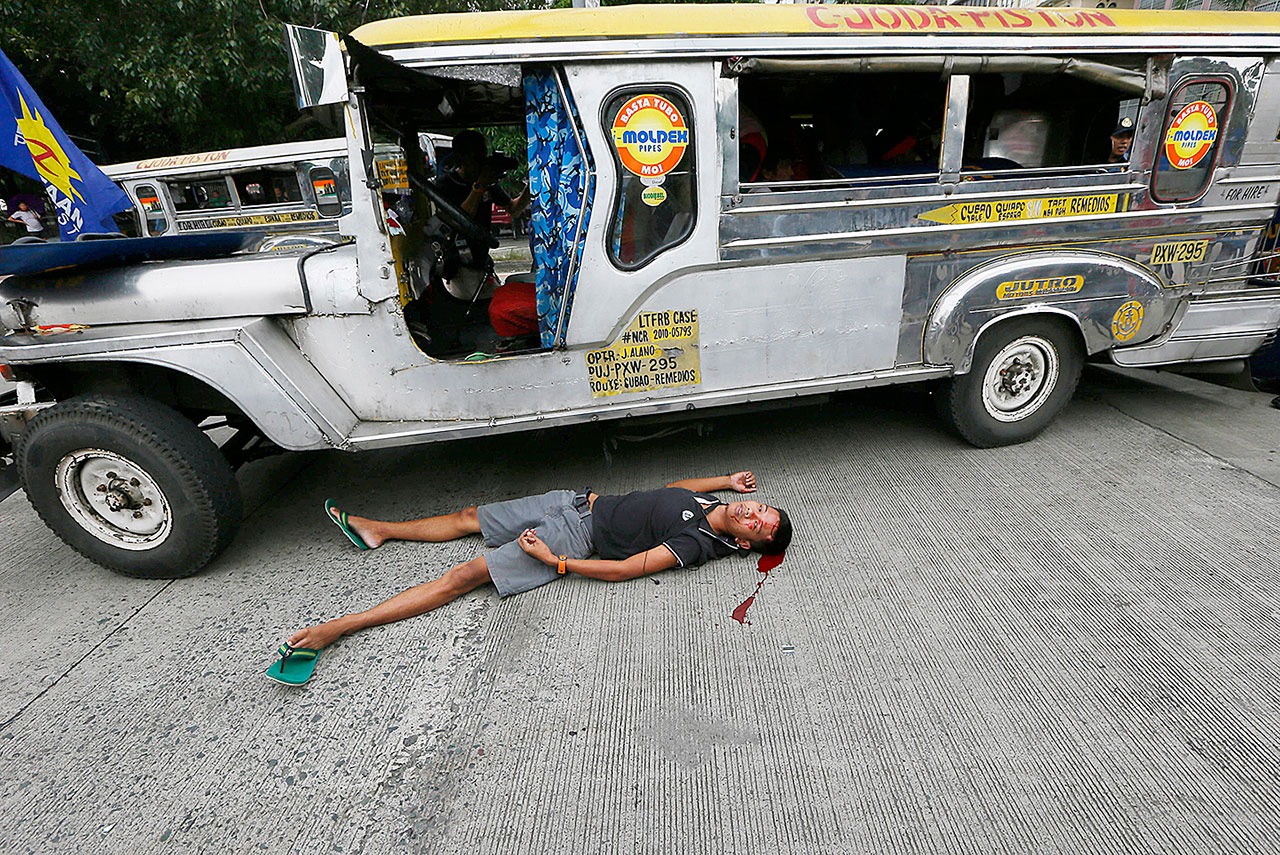 A bloodied protester lies next to a passenger vehicle after he was injured in a violent dispersal outside the U.S. Embassy in Manila, Philippines on Wednesday, Oct. 19. A Philippine police van rammed into protesters, leaving several bloodied, as an anti-U.S. rally turned violent Wednesday at the embassy. (AP Photo/Bullit Marquez)