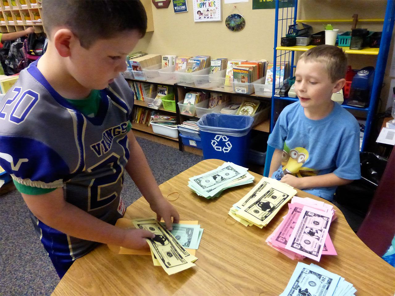 Artemis Batchelor, right, pays out classmate Cooper Rysemus’ earnings in Froggy Dollars in Lisa Holland’s classroom at Mount Pilchuck Elementary School in Lake Stevens on Sept. 30. It was “payday” at the class bank, part of a yearlong financial education project by Holland that culminates in a student marketplace. (Contributed photo)