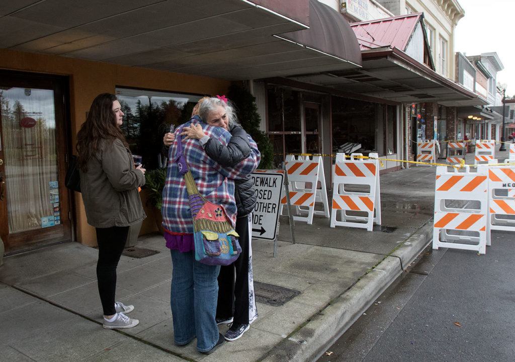 Thoughtful Israel hug 2 Bits and More owner Dawn Ambler on the sidewalk beside the burned out remains of the indoor flea market and thrift shop on Tuesday, Oct. 25, 2016 in Arlington, Wa. At left is Ambler’s niece Jeness Crtiz. (Andy Bronson / The Herald)
