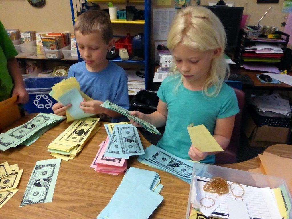 Artemis Batchelor, left, and Andi Elshaug serve as bankers, handing out Froggy Dollars to classmates in Lisa Holland’s classroom at Mount Pilchuck Elementary School in Lake Stevens on Sept. 30. It was “payday” at the class bank, part of a yearlong financial education project by Holland that culminates in a student marketplace. (Contributed photo)
