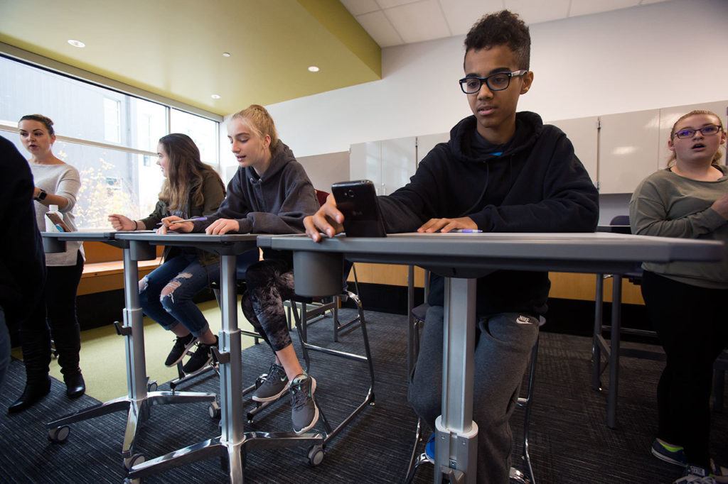 Leota Junior High eighth grader A.J. Springer places his cell phone in a grove in a stand-up/sit down desk as he and other students test out different chairs and desks at North Creek High School on Wednesday, Oct. 19, 2016 in Bothell, Wa. The students tested and graded three different sets of chairs and desks that the Northshore School District may purchase for the new high school. (Andy Bronson / The Herald)
