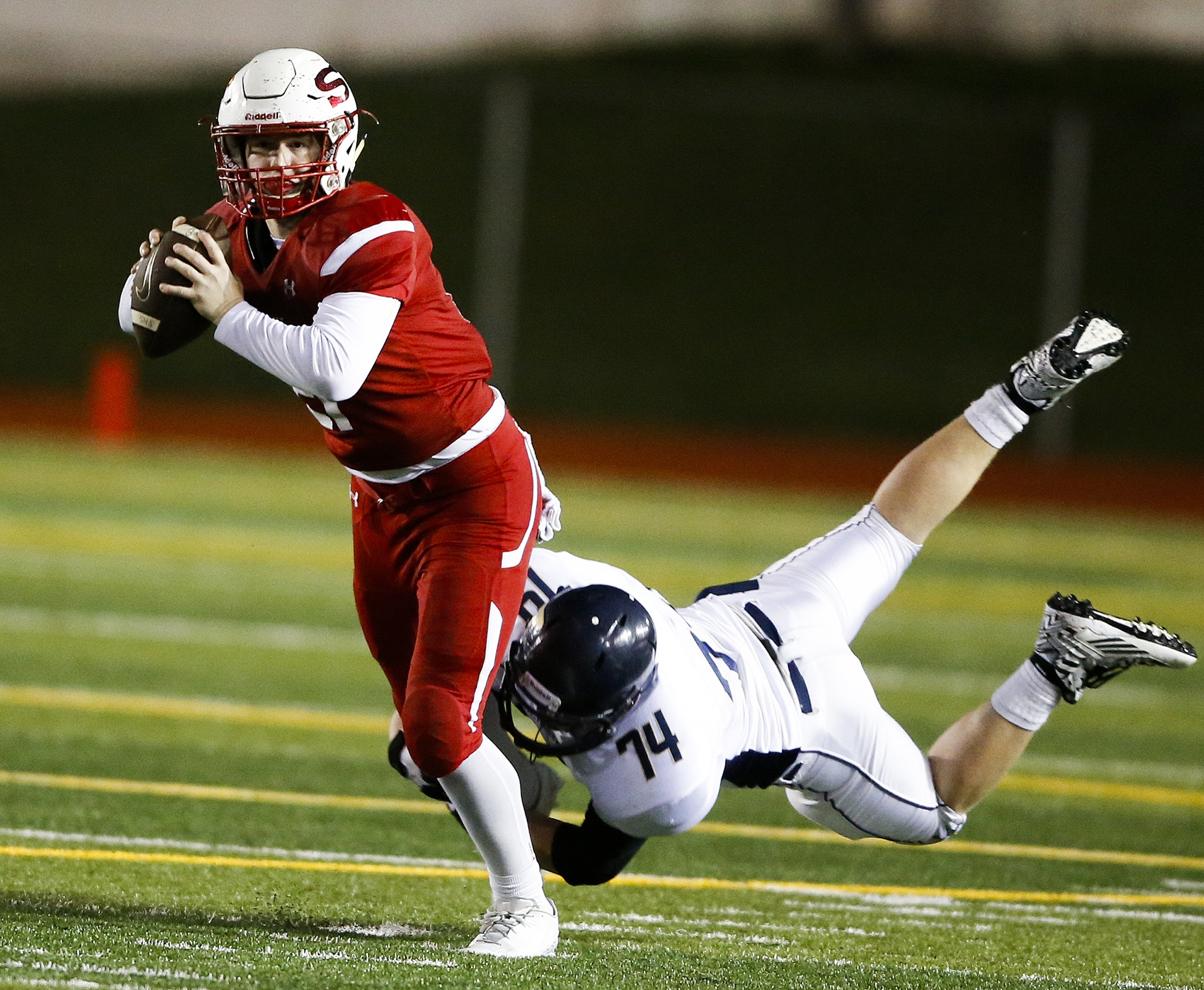 Snohomish quarterback Brandon Jodock (left) looks to pass as he’s wrapped up by Arlington defender Logan Cartwright during a district play-in game Tuesday at Snohomish High School. (Ian Terry / The Herald)