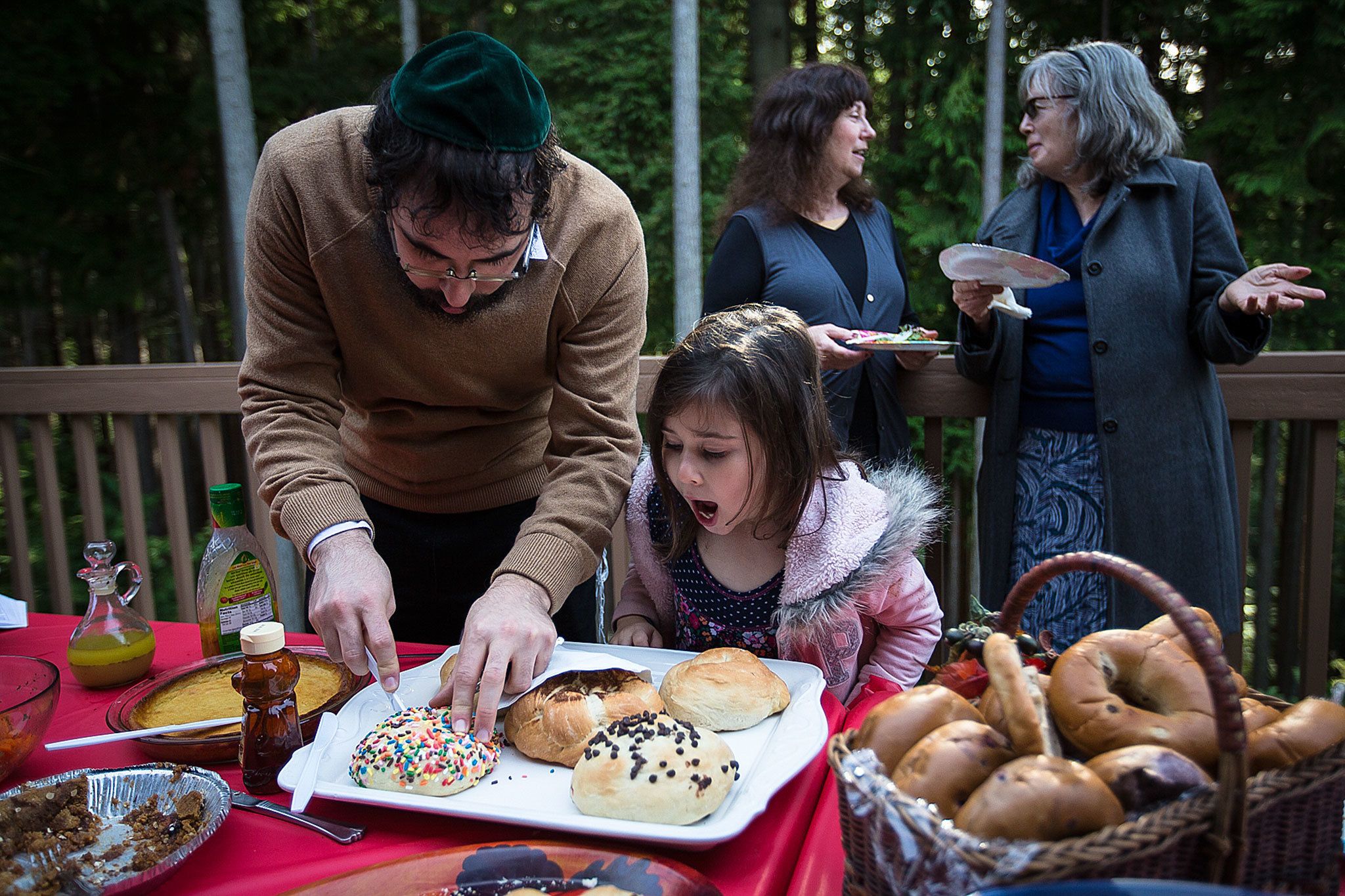 Chaya Paltiel, 5, watches as her dad, Rabbi Berel Paltiel, slices a piece of challah during a celebration of the Jewish Festival of Sukkot hosted by Iris Shamas at her home in Lynnwood on Oct. 23. Shamas and her husband, Richard, host regular gatherings with their friends to celebrate Jewish holidays and traditions. (Daniella Beccaria / For The Herald)