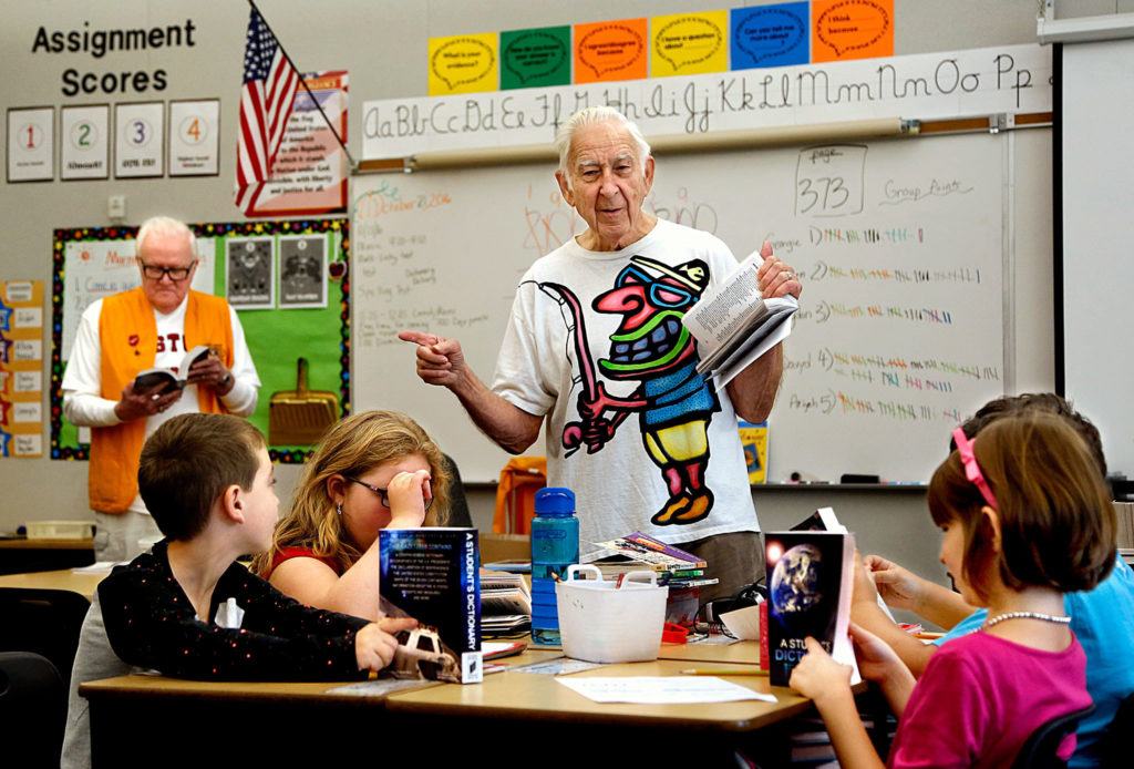 James Henry (back left) looks in one of the new dictionaries while Jack Lapoint (center) tells Silver Lake Elementary School third-graders in Christi Castro’s class about some of the amazing information available in a dictionary, after the two Kiwanis Club members gave them new dictionaries. It was the final dictionary giveaway by the organization, which recently voted to disband because there aren’t enough members. (Dan Bates / The Herald)
