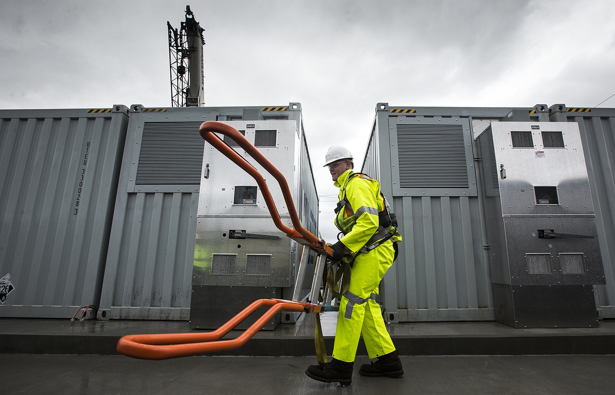 Alex Weenink, lead field technician for the Snohomish County Public Utility District, carries a ladder after his crew finished hoisting 20 new vanadium flow batteries into place at the Everett Substation on Wednesday. Mukilteo-based UniEnergy Technologies made the units, which will allow for the PUD to better handle peak usage by storing energy in the big batteries. (Ian Terry / The Herald)