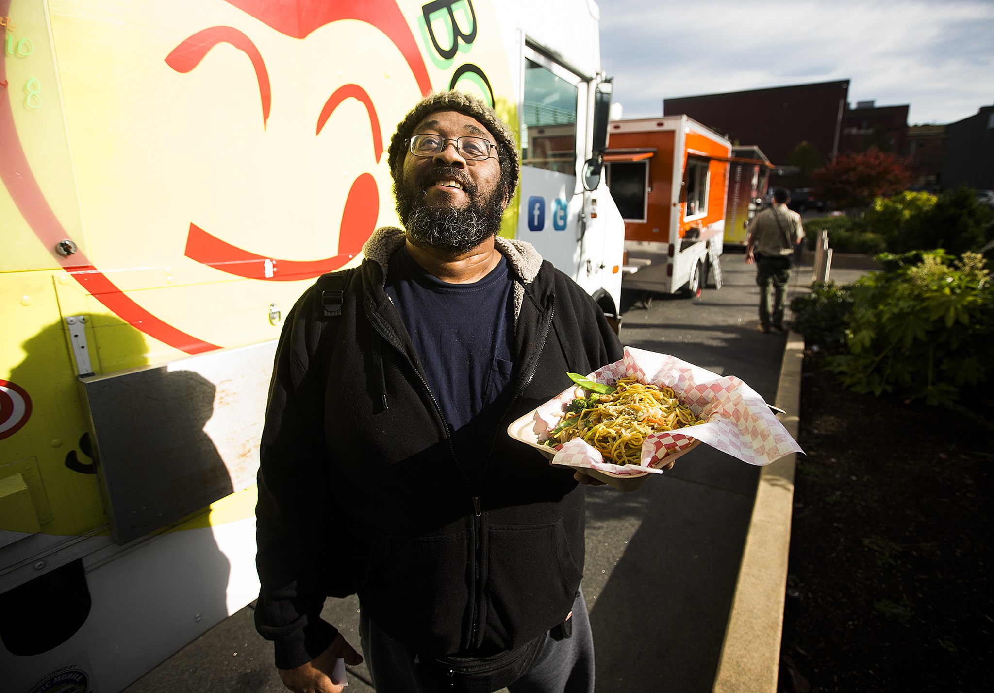 Kevin Hughes stands near the Yummy Box Food Truck after picking up his order of chicken stir fry on Friday afternoon in Everett. “I got off the bus and my nose led me here,” Hughes said. Three Snohomish County-based food trucks will share a space near the Everett Performing Arts Center each Friday at lunch time as part of a year-long pilot project with the city. (Ian Terry / The Herald)