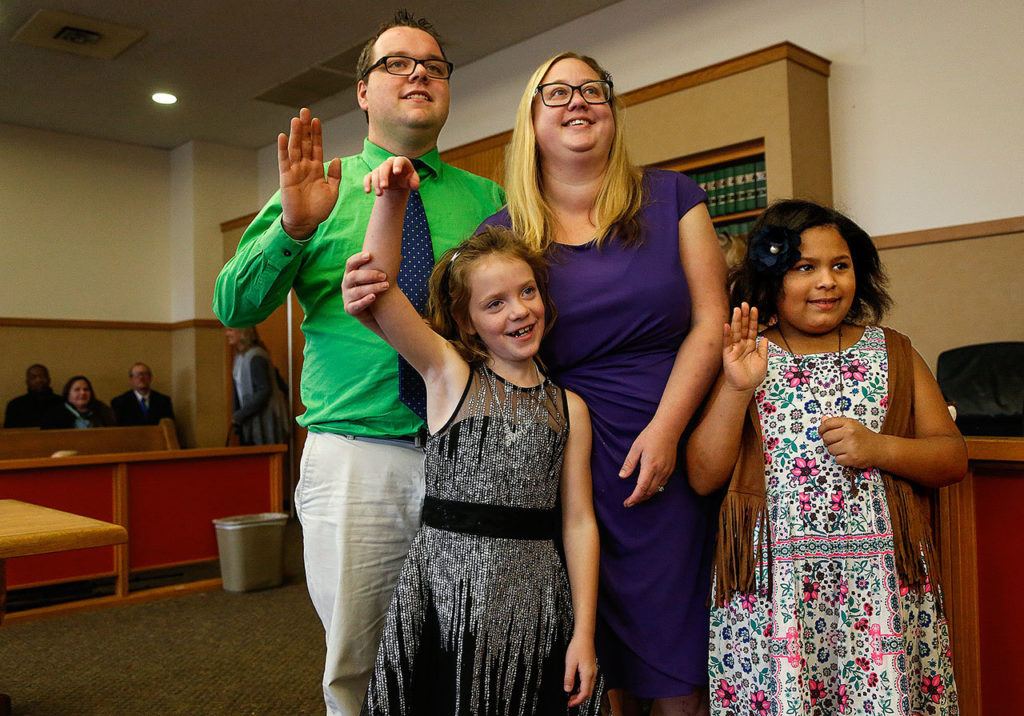 Nick and Erin Schramm gladly raise their right hands (and Miah’s) before Superior Court Judge David A. Kurtz on Friday morning as they adopt Kortnei, 9 (right) and Miah, 8, making them a very happy family of four. (Dan Bates / The Herald)
