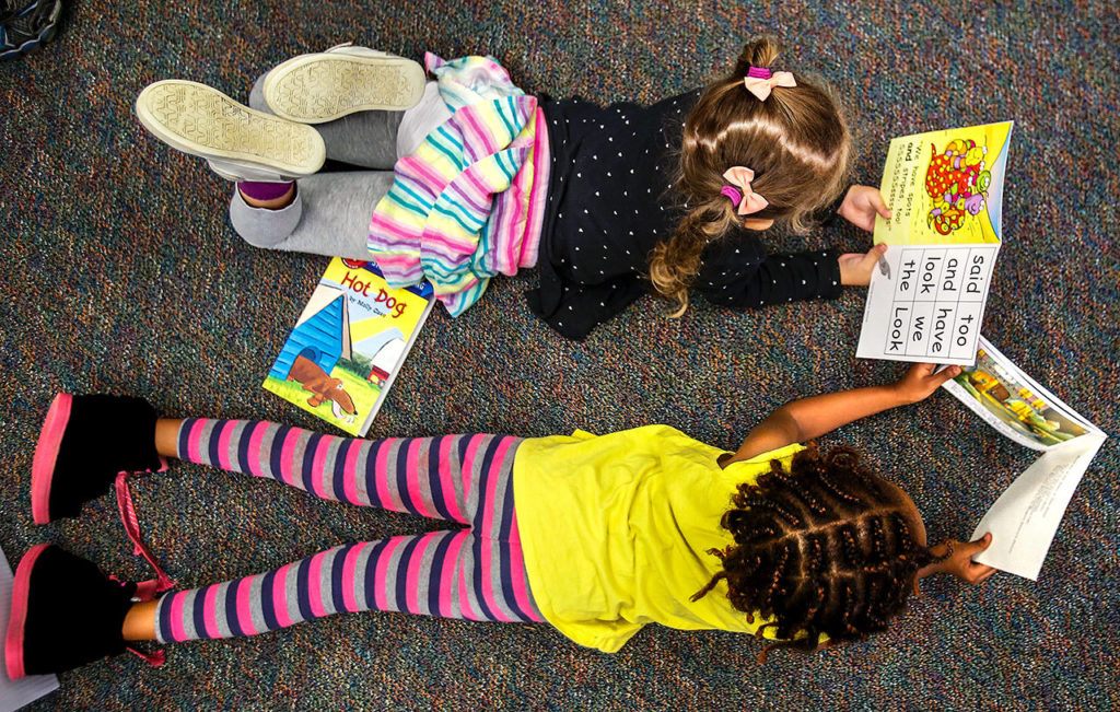 Mercy Mathews (bottom) and Lily Holt get comfortable and start reading the new books. (Dan Bates / The Herald)
