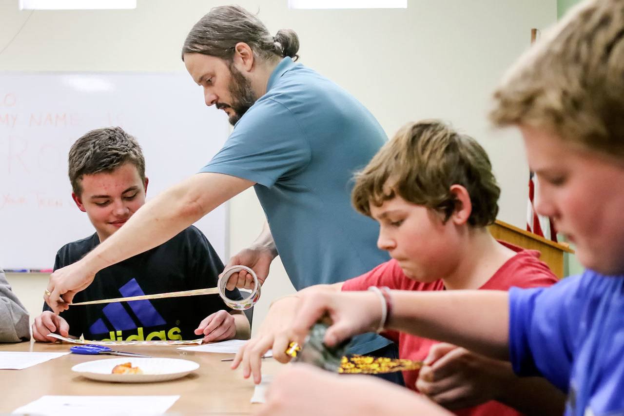 (From left) Damien Field, 13, gets help from Rob Branigin as Layne Seay, 12, and Calvin Drake, 12, make duct tape wallets at Stanwood Library on Oct. 28. (Kevin Clark / The Herald)