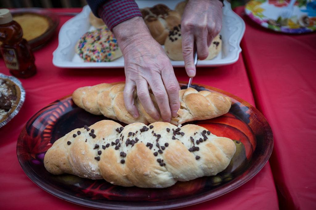 An attendee slices a piece of challah, traditional bread, during a celebration of the Jewish Festival of Sukkot hosted by Iris Shamas at her home in Lynwood on Sunday, Oct. 23. Shamas bakes the bread in the traditional form (pictured) and a round shape with various sweet toppings. (Daniella Beccaria / For The Herald)
