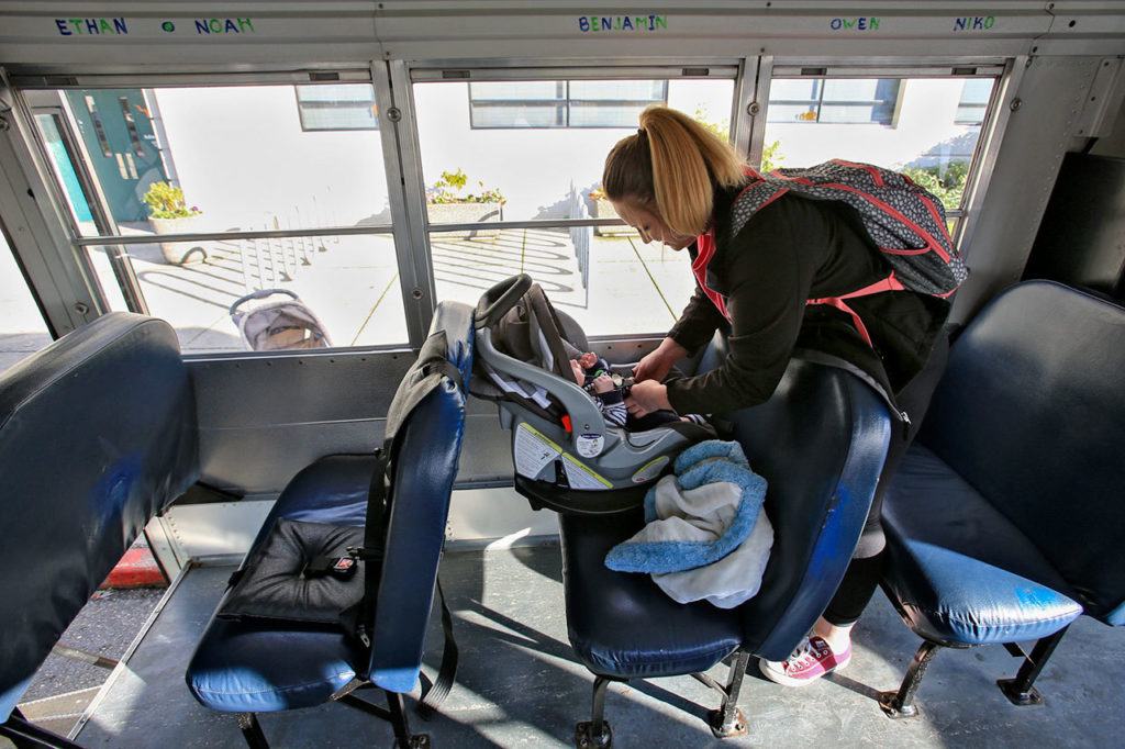 Jessiana King buckles her son, Brayden Varnes, into a car seat aboard the baby bus after school at Crossroads High in Granite Falls. Currently, King is the only student on the bus for the 7-minute ride home. (Kevin Clark / The Herald)
