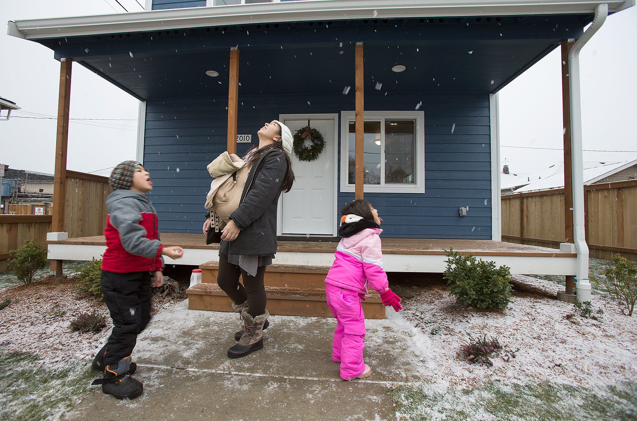 With her infant son, Matias, on her chest, Sandy Flores enjoys falling snow Saturday with her son, Ray J., and daughter, Sasha, in front of their new home in Everett. Flores, her husband, Ray, and their three young kids became the new owners of Phoenix II, a house in North Everett from Habitat for Humanity of Snohomish County. They contributed more than 500 hours of sweat equity in the construction of the home. (Andy Bronson / The Herald)