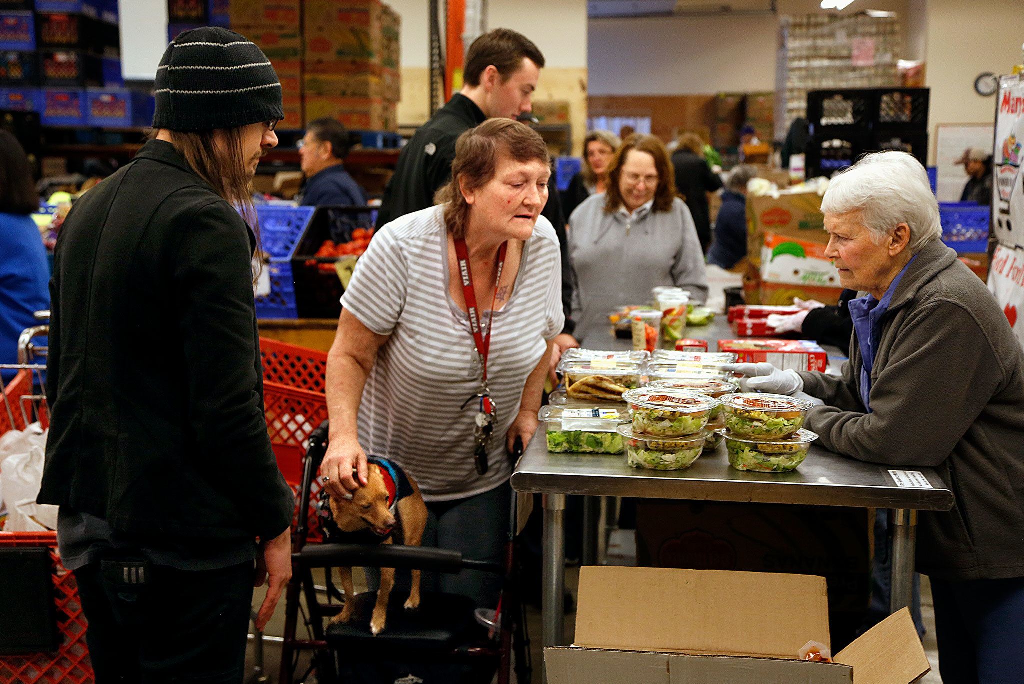 Assisted by volunteers, Adam Szydel (left) and Marge Beauchamp (right), Kerrin Thompson, of Marysville, picks out a few items at the Marysville Food Bank, just days before Thanksgiving. Thompson was also able to get something for her small service dog, Diego. (Dan Bates / The Herald)