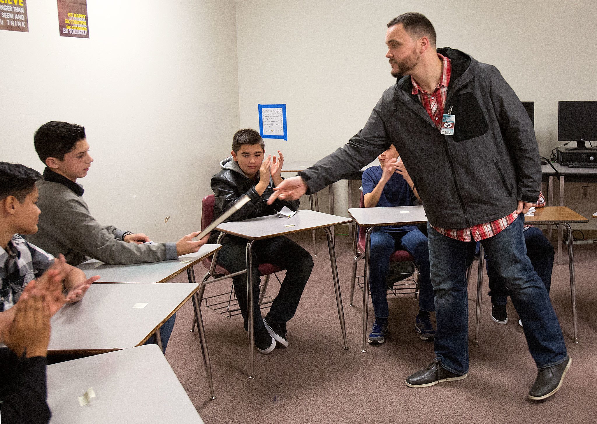 Classmates clap as Jake Marsh hands seventh-grader Adrian Seeker his personal copy of the book “A Hand to Guide Me,” written by Denzel Washington about mentors, after the group graduated from the “Passport to Manhood” program at Voyager Middle School in Everett on Tuesday. (Andy Bronson / The Herald)
