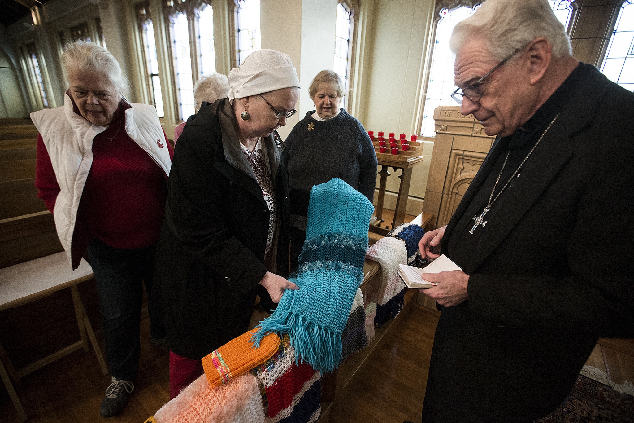 Pastor Wayne Bond (right) looks over shawls handmade by the Trinity Episcopal knit and crochet group including members Barbara Linvog (center left) and Brenda Congdon (left) at the Everett church Nov. 29. (Ian Terry / The Herald)