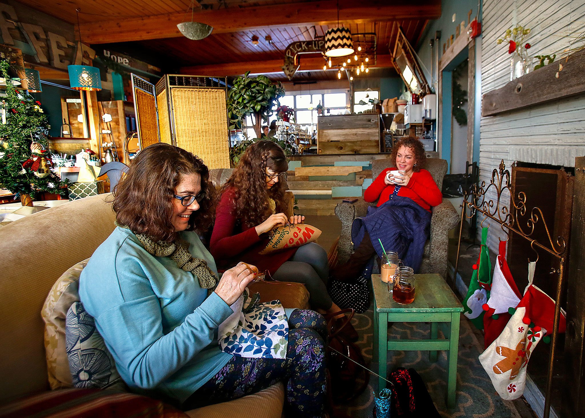 Friends Lynn Devoe (left), from Snohomish, Chloe Wilcox, from Lake Stevens, and Tina Roberts (right), from Lake Stevens, sit by the warmth of a fireplace drinking coffee, talking and crafting Wednesday morning at the Living Room Coffee House at 1636 Fourth St. in Marysville. (Dan Bates / The Herald)