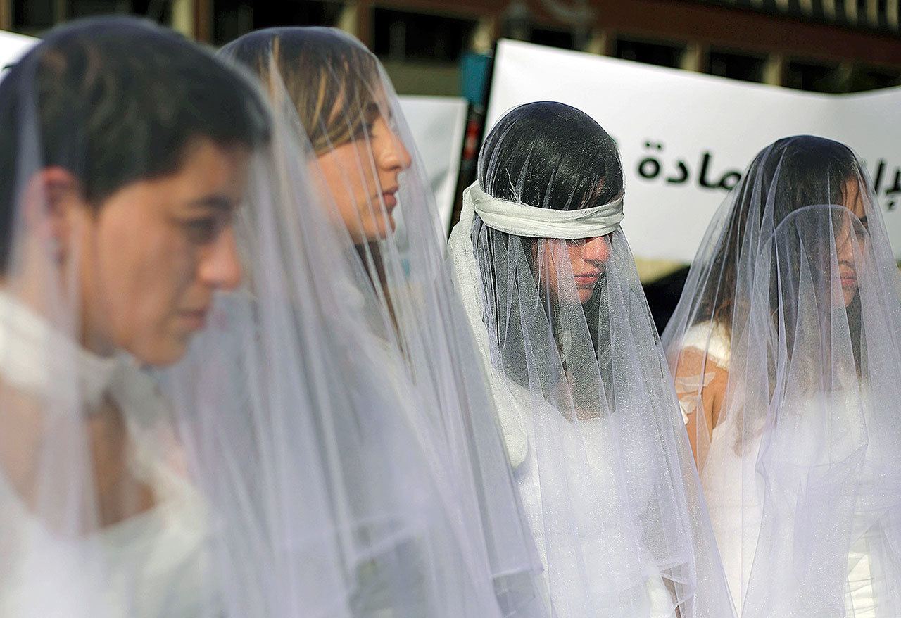 A dozen Lebanese women, dressed as brides in white wedding dresses stained with fake blood and wearing bandages, stand in front of the government building in downtown Beirut, Lebanon, on Tuesday, Dec. 6. The activists are protesting a Lebanese law that allows a rapist to get away with his crime if he marries the survivor. (AP Photo/Bilal Hussein)