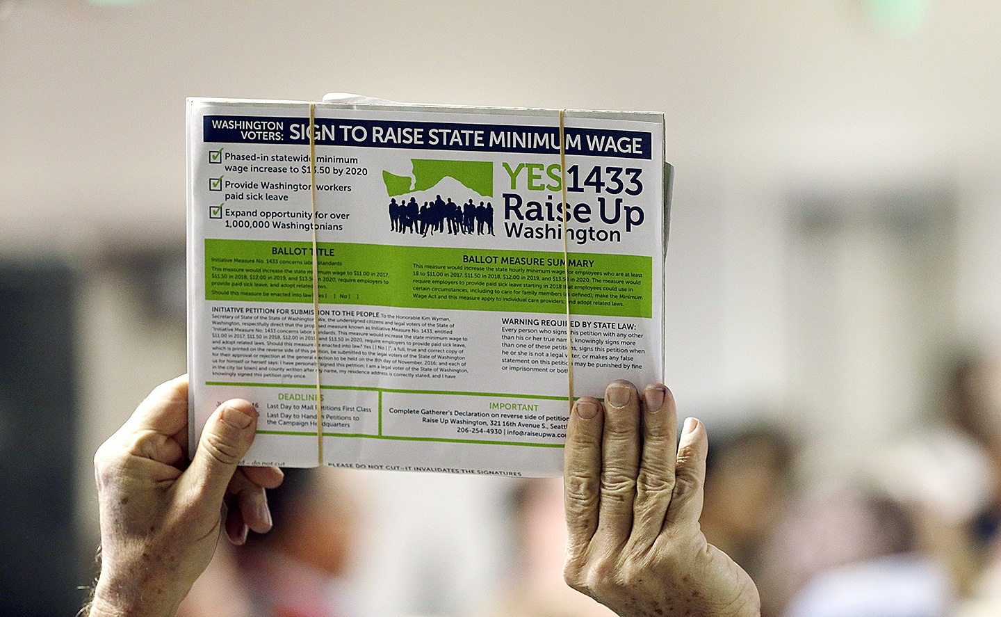 In this March 22, 2016, photo, a supporter holds up a petition for Initiative 1433, a ballot measure to raise Washington state’s minimum wage and allow all workers in the state to earn paid sick leave, in Everett, Washington. The passage of the minimum wage hike was among the top news stories in Washington in 2016. (AP Photo/Elaine Thompson, File)