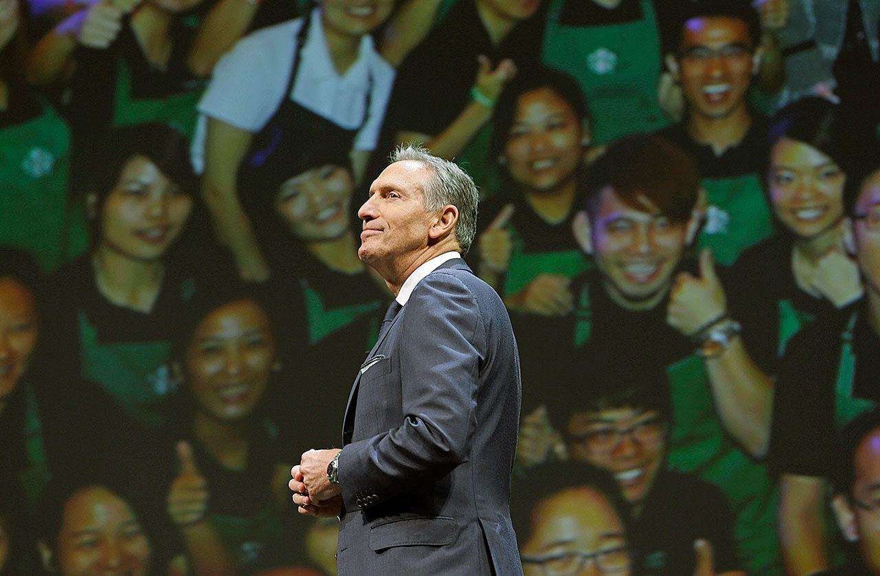 In this March 23, 2016, photo, Starbucks CEO Howard Schultz walks in front of a photo of Starbucks baristas at the coffee company’s annual shareholders meeting in Seattle. Starbucks announced Thursday, Dec. 1, that Schultz is stepping down from the coffee chain that he joined more than 30 years ago, and that Kevin Johnson will become chief executive as of April 3, 2017. (AP Photo/Ted S. Warren, File)