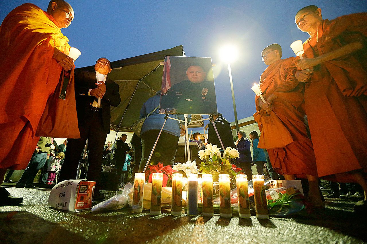Monks from the Khmer Theravadin Buddhist Association of Tacoma hold candles next to a photo of Tacoma Police Officer Reginald “Jake” Gutierrez during a vigil, Thursday, Dec. 1, in Tacoma. Gutierrez was shot while responding to a domestic violence call Wednesday, Nov. 30, and died later in the day at a hospital. (AP Photo/Ted S. Warren)