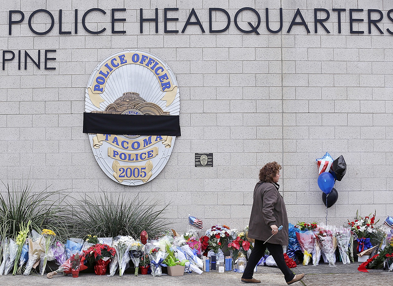 A visitor walks past the growing memorial at Tacoma Police Headquarters on Thursday, Dec. 1, in memory of Tacoma Police Officer Reginald “Jake” Gutierrez. Gutierrez was shot while responding to a domestic violence call Wednesday and died later in the day at a hospital. (AP Photo/Ted S. Warren)