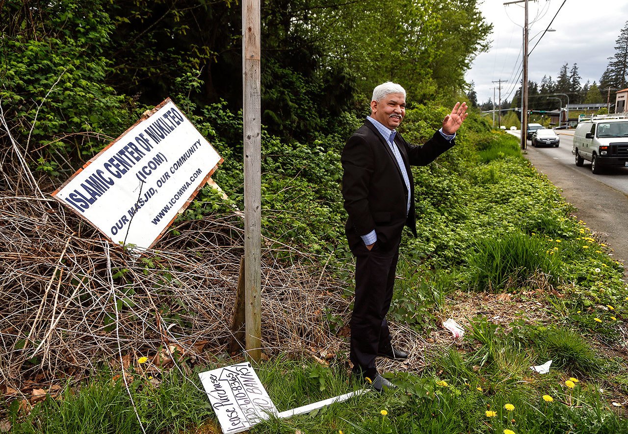 Mohammed Riaz Khan waves at a passerby he knows near the intersection of Harbour Point Blvd. and Mukilteo Speedway, while visiting the site of the planned mosque, The Islamic Center of Mukilteo, in early May. The signage, which had fallen or was blown down, is at the east end of the property. (Dan Bates / Herald file)