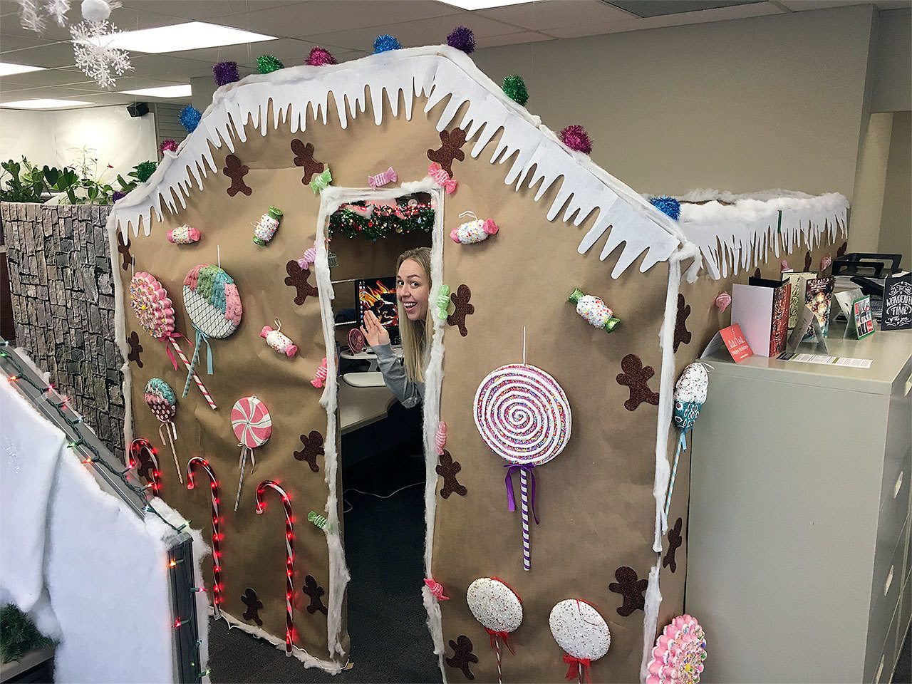 Insurance Services Group employee Marie Boughton peeks out from her gingerbread house. The Christmas cubicle contest was part of a festive season at the Edmonds company, which also collected gift cards for Washington Kids in Transition. (Contributed photo)