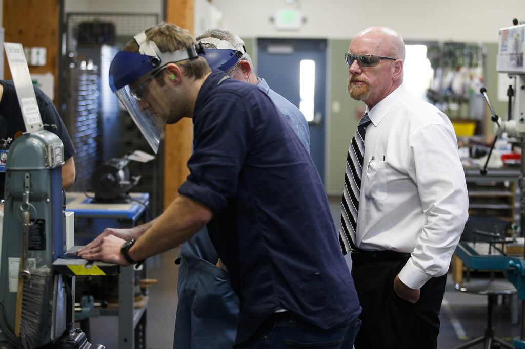 Larry Cluphf (right), executive director at the Washington Aerospace Training & Research Center, watches as students work with a belt sander at the Everett facility on Dec. 16. (Ian Terry / The Herald)
