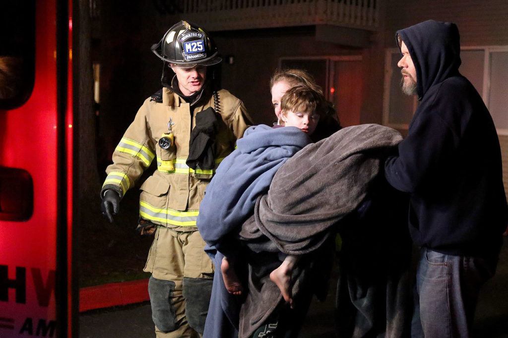 Victoria Troupe holds her son, Henry, then 6, as she and her husband, Sean, are helped into an ambulance during the Bluffs apartment fire. The Troupes lost most of their possessions and their family pets. (Kevin Clark / Herald file)
