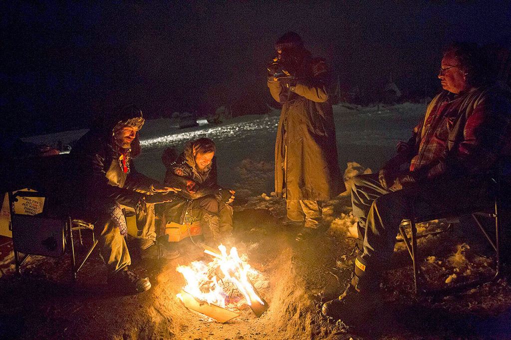 Phillip Swafford, from left, and David Cook, both of Colorado, sit around a campfire at the Oceti Sakowin camp where thousands have gathered to protest the Dakota Access oil pipeline near Cannon Ball, North Dakota, on Wednesday, Nov. 30. The pipeline is designed to carry oil from North Dakota to Illinois. Opponents, including the Standing Rock Sioux tribe, say it will harm drinking water and cultural sites. (AP Photo/David Goldman)
