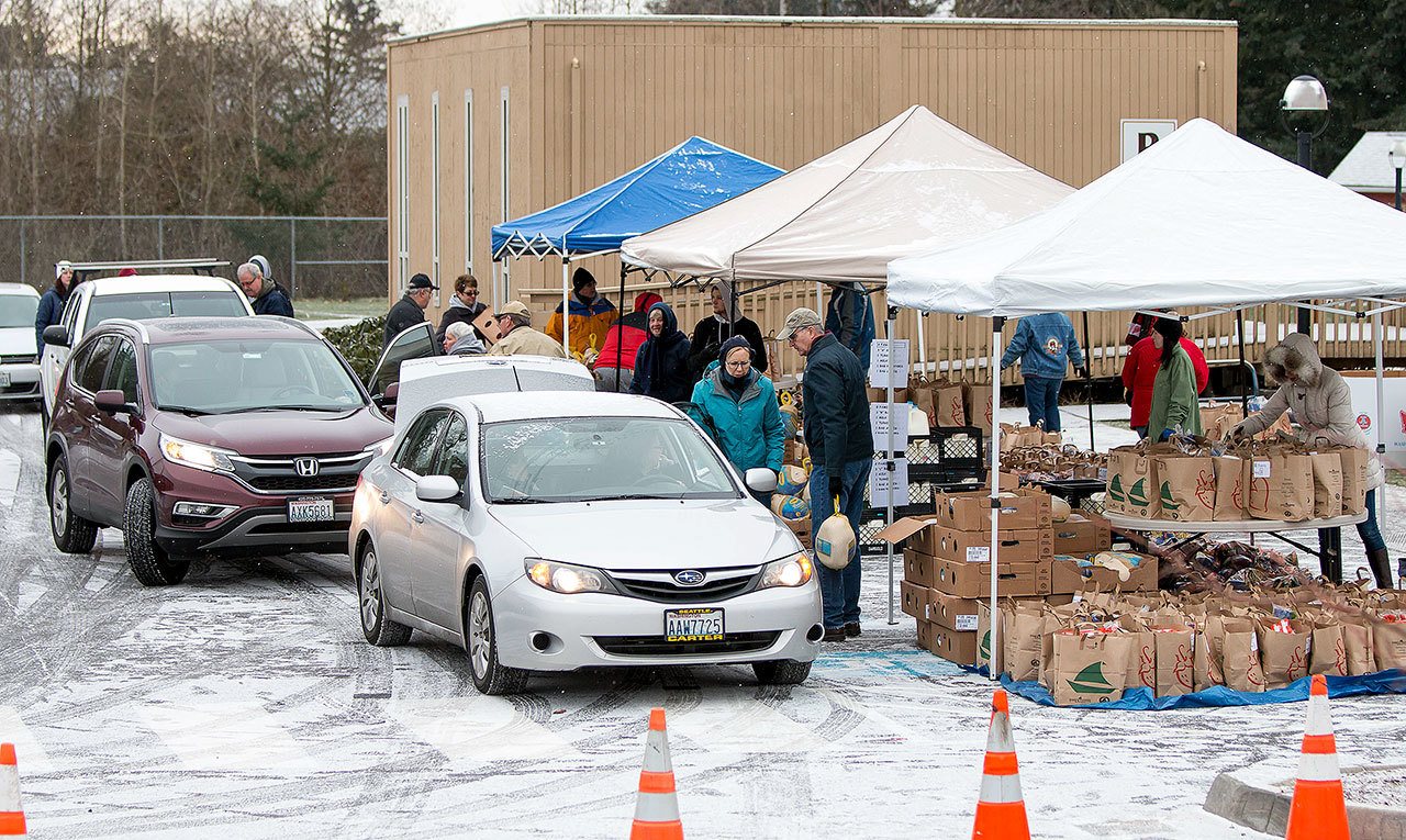 Volunteers load up on food items to deliver to families in need around the Mill Creek and south Everett area. Cars lined up behind the church and waited to stop at three loading stations where bags of food, milk and frozen turkeys were provided. (Bill Trueit / For the Herald)