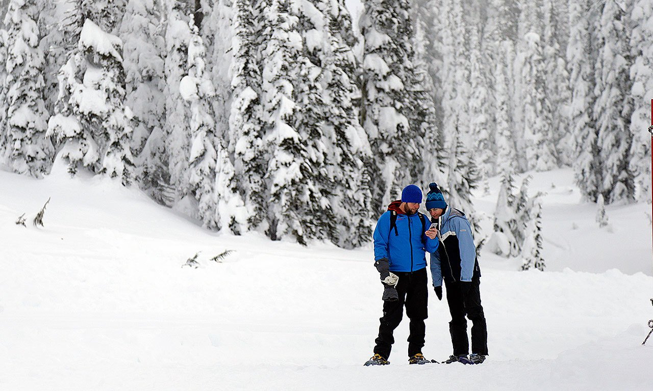 In this photo taken Friday, Dec. 16, snowshoers look at a cellphone while in the backcountry near the Paradise area at Mount Rainier National Park. Spotty or no cellular service has been the norm at the nation’s fifth oldest park south of Seattle, but that could change soon. Mount Rainier National Park is considering proposals to provide cellular service in the park, setting off debates about whether people enjoying the park and surrounding wilderness areas should have access to calls and social media while in nature. (AP Photo / Elaine Thompson)