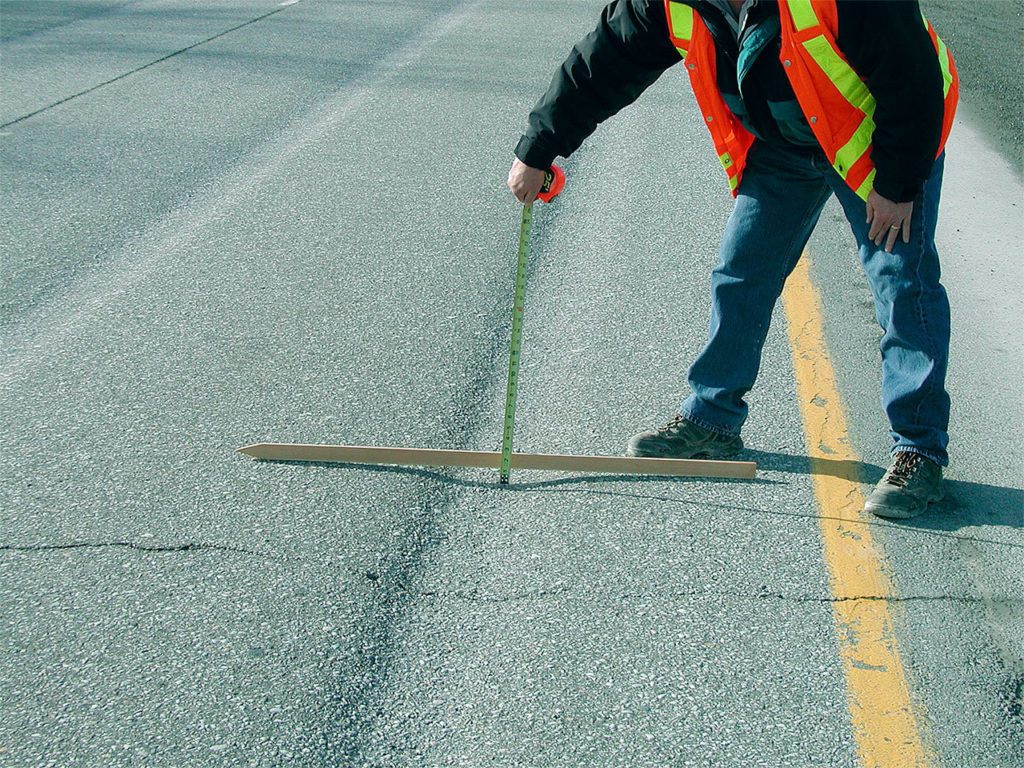 A state worker measures the extent of rutting in a highway, damage caused primarily by studded tires over the years. (WSDOT photo)
