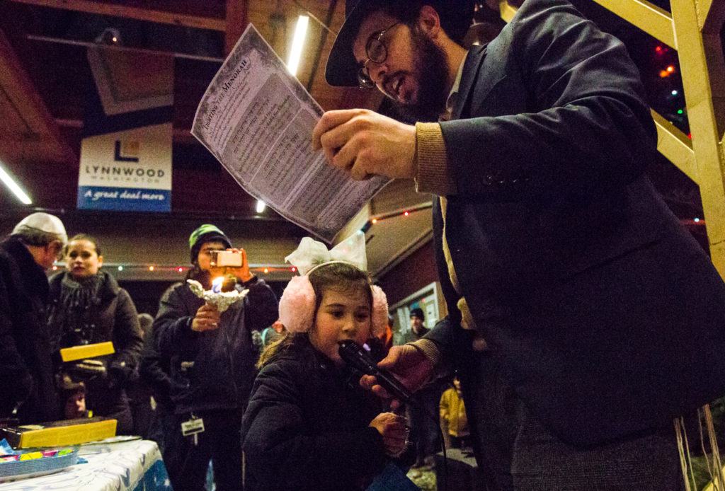 Rabbi Berel Paltiel holds the microphone so his 5-year-old daughter, Chaya Paltiel, can sing Hanukkah songs during the fifth annual public menorah lighting ceremony at Lynnwood City Hall on Monday. About 100 people gathered to sing, eat and celebrate the third night of Hanukkah. (Daniella Beccaria / The Herald)
