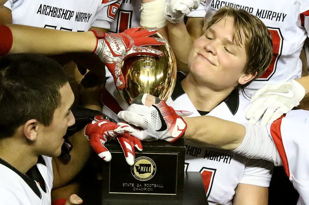Archbishop Murphy quarterback Connor Johnson (right) and teammates admire the trophy after beating Liberty 56-14 in the Class 2A state championship game Saturday afternoon at the Tacoma Dome. (Kevin Clark / The Herald)
